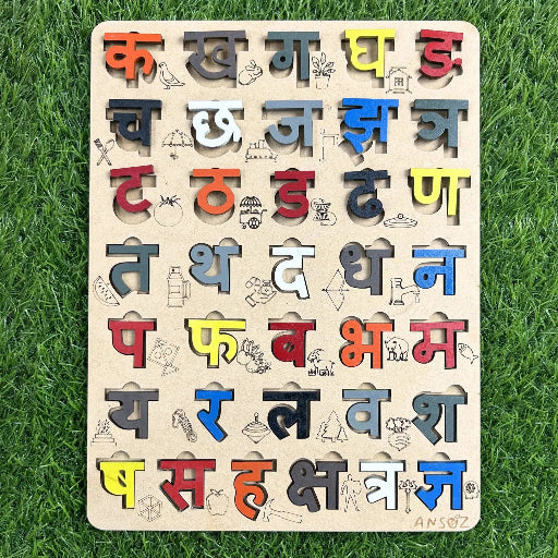 A wooden Hindi varnamala puzzle board, its colorful letters paired with matching pictures, sits on the grass.