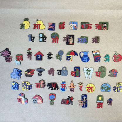 A collection of colorful Devanagari script alphabet stickers or pins arranged in rows on a light beige textured background.