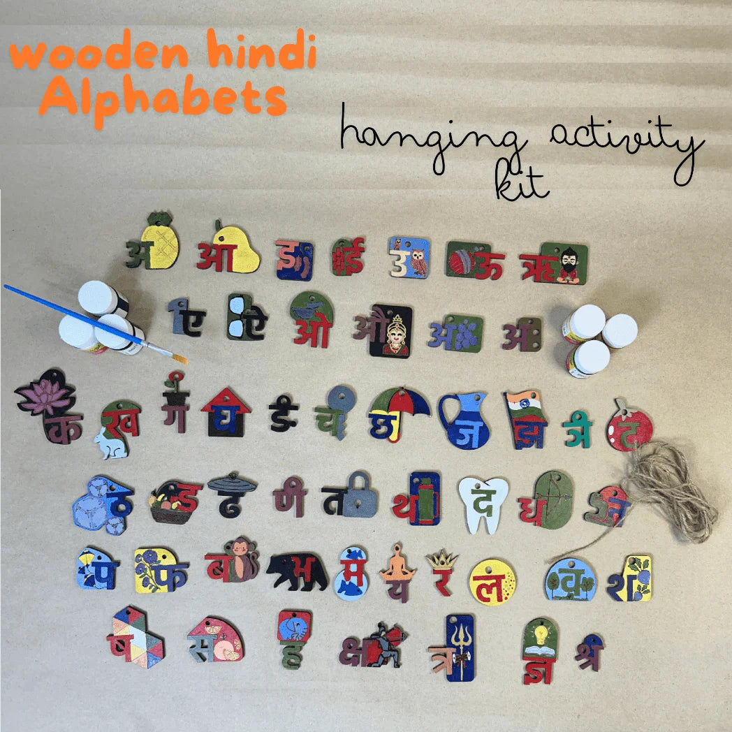 A wooden Hindi alphabet hanging activity kit arranged on a beige textured background, with orange text reading 'wooden hindi Alphabets' and black script text reading 'hanging activity kit.' The kit includes many colorful wooden Hindi letters shaped like everyday objects, small hanging pegs, a paintbrush, two small bottles, and a string.