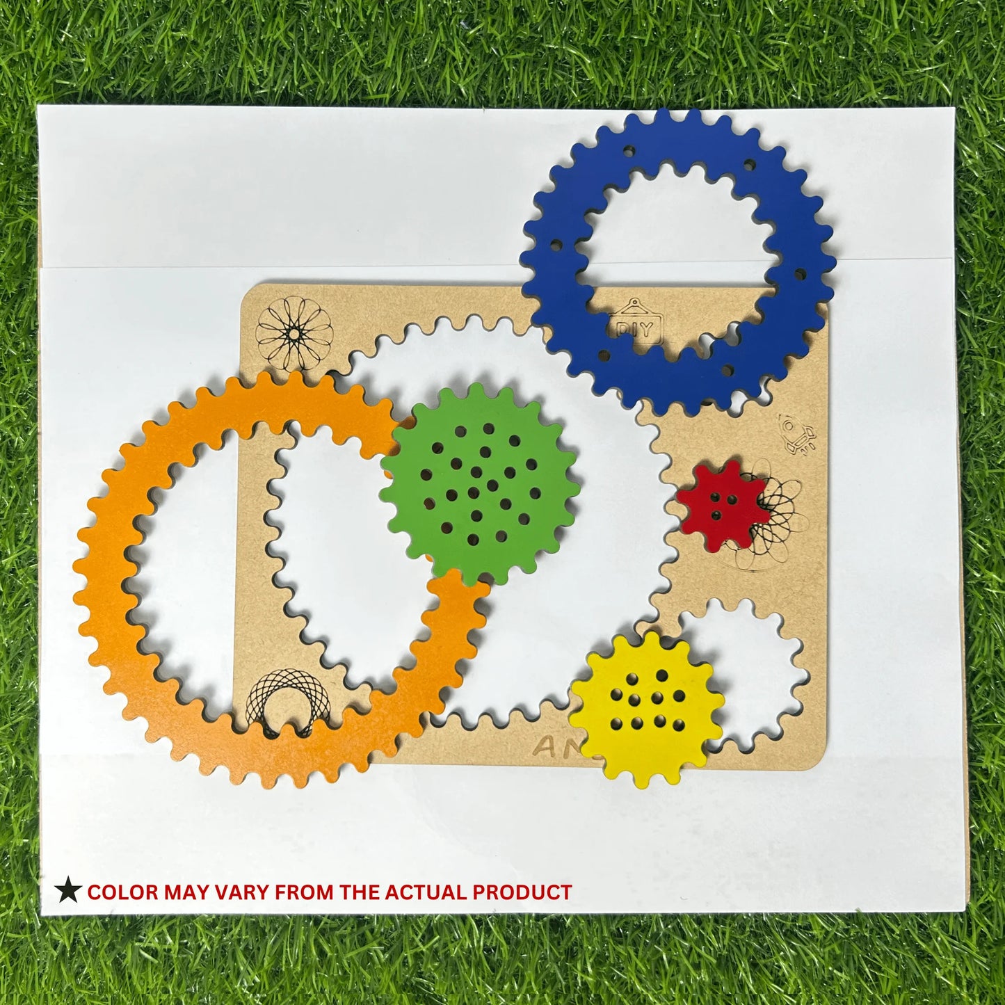 A children's wooden gear puzzle set with colorful interlocking gears in blue, orange, green, red, and yellow, displayed on a white backing card over a green grass background.