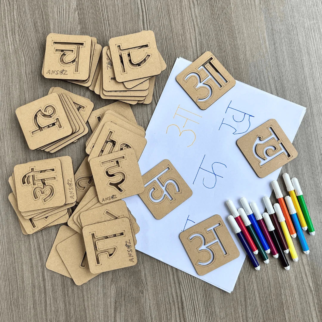 A set of wooden Hindi learning stencil board arranged on a light wood surface, with a white worksheet, colored markers, and additional scattered cards.