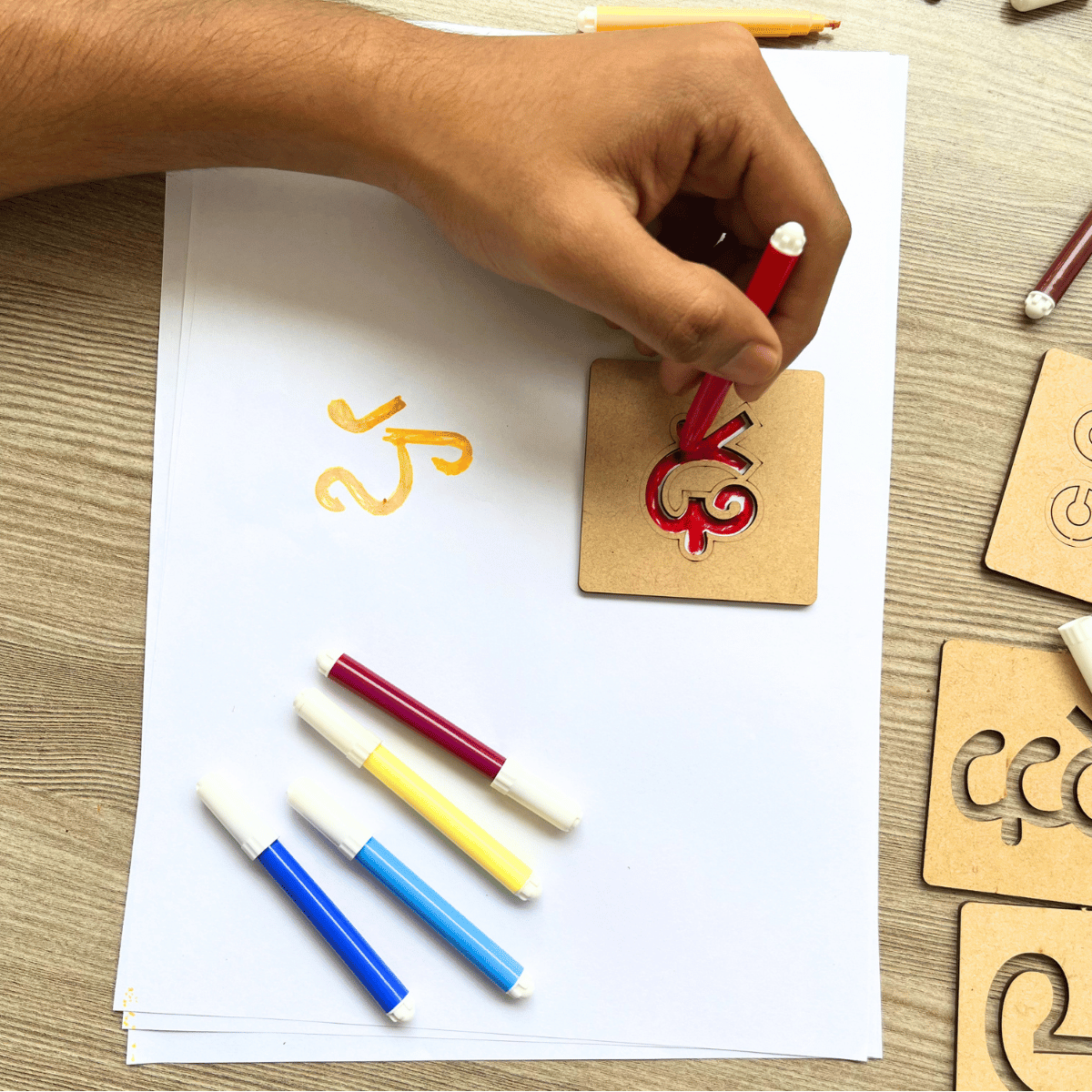 Kid practicing writing Telugu alphabet letters using stencil and sketch pens.