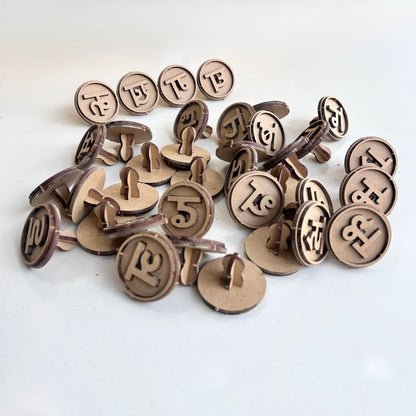 Multiple wooden Hindi vowel and consonant stamps scattered on a white surface. The educational stamp set includes Hindi Swar and Vyanjan letters designed to help children learn Hindi alphabet recognition, letter formation, and language skills through play.