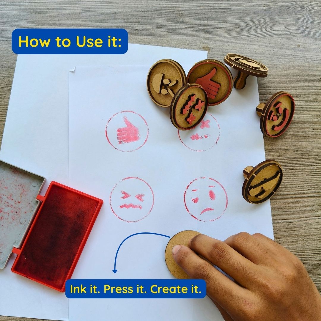 Hand pressing a cute emoji stamp onto paper with an ink pad for fun DIY art.
