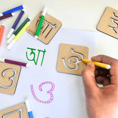  Child tracing Assamese alphabet letters using reusable wooden stencil kit with colorful sketch pens, promoting handwriting, creativity, and early Assamese language learning.