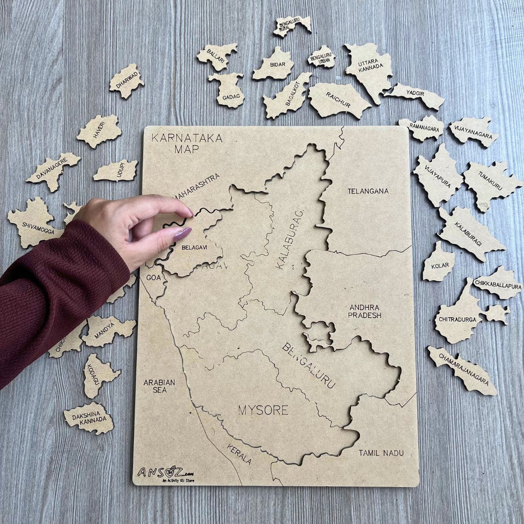 Hand placing district piece on Karnataka map puzzle with all pieces spread around the board