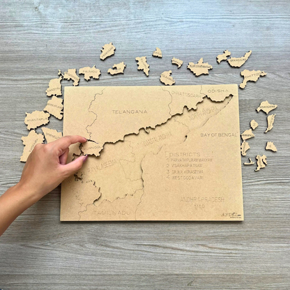 Hand placing district pieces on a wooden Andhra Pradesh map puzzle.