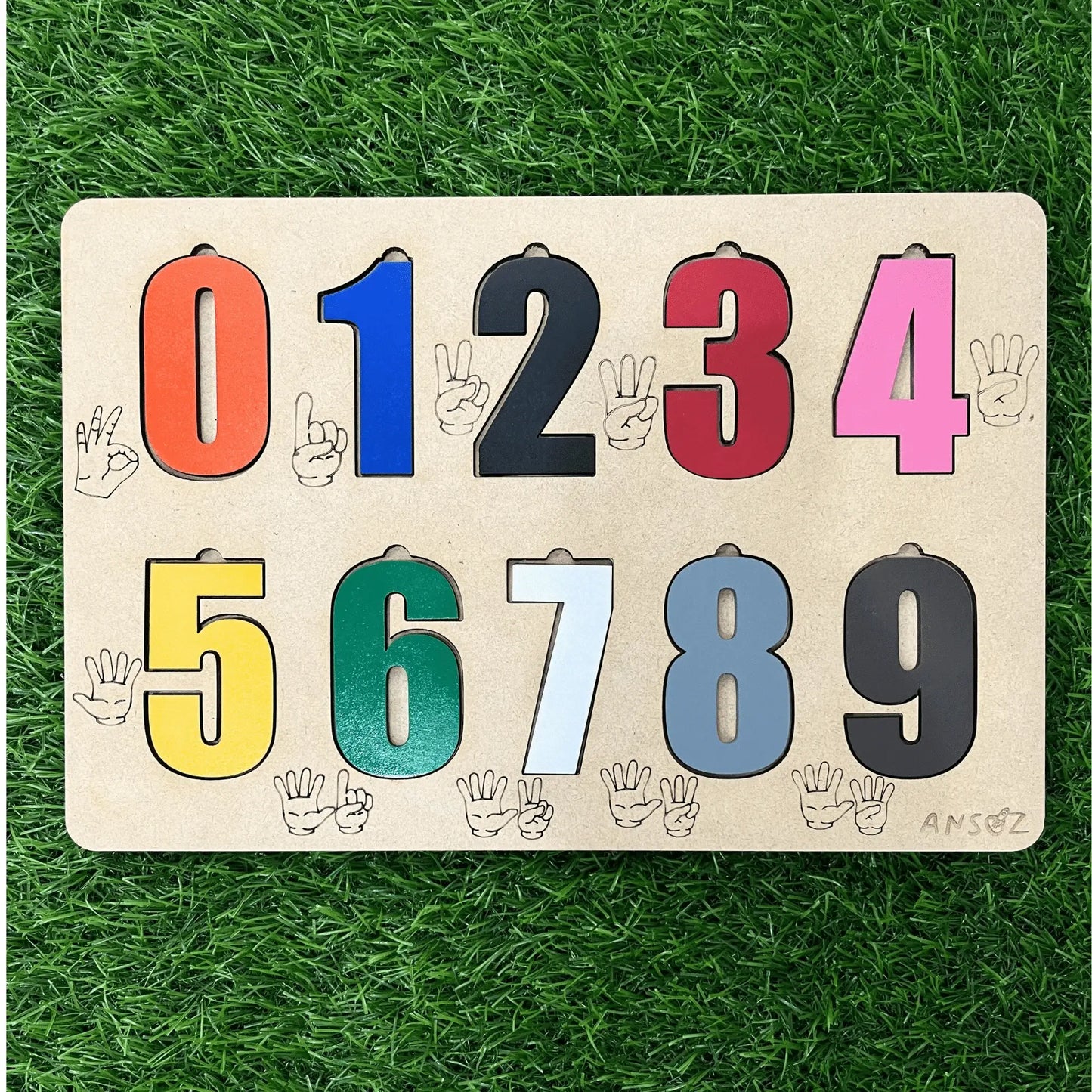 A wooden educational number puzzle board featuring numbers 0 through 9 in colorful shapes, placed on a green artificial grass background.