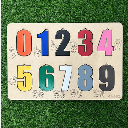 A wooden educational number puzzle board featuring numbers 0 through 9 in colorful shapes, placed on a green artificial grass background.