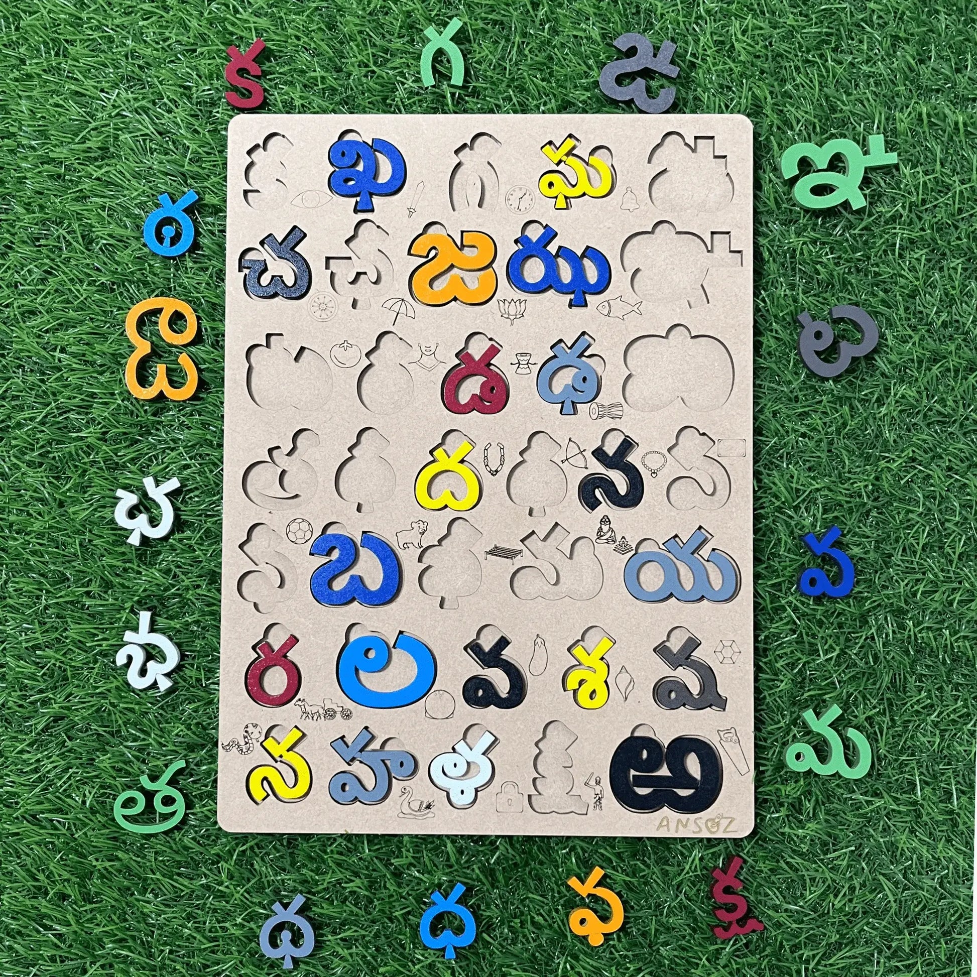A wooden puzzle board featuring cutout shapes and colorful Telugu letters arranged around it on a green grass-like surface.
