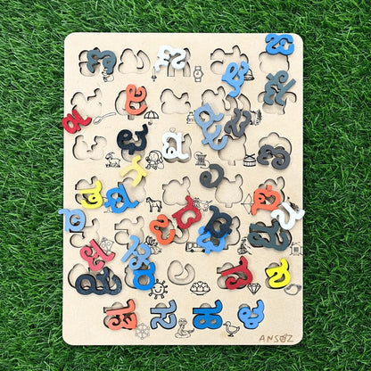 A wooden alphabet puzzle board with colorful letter pieces scattered on a green grass-like background. The board has cutout letters and small illustrated shapes, and the brand name 'ANSOZ' is visible in the bottom right corner.