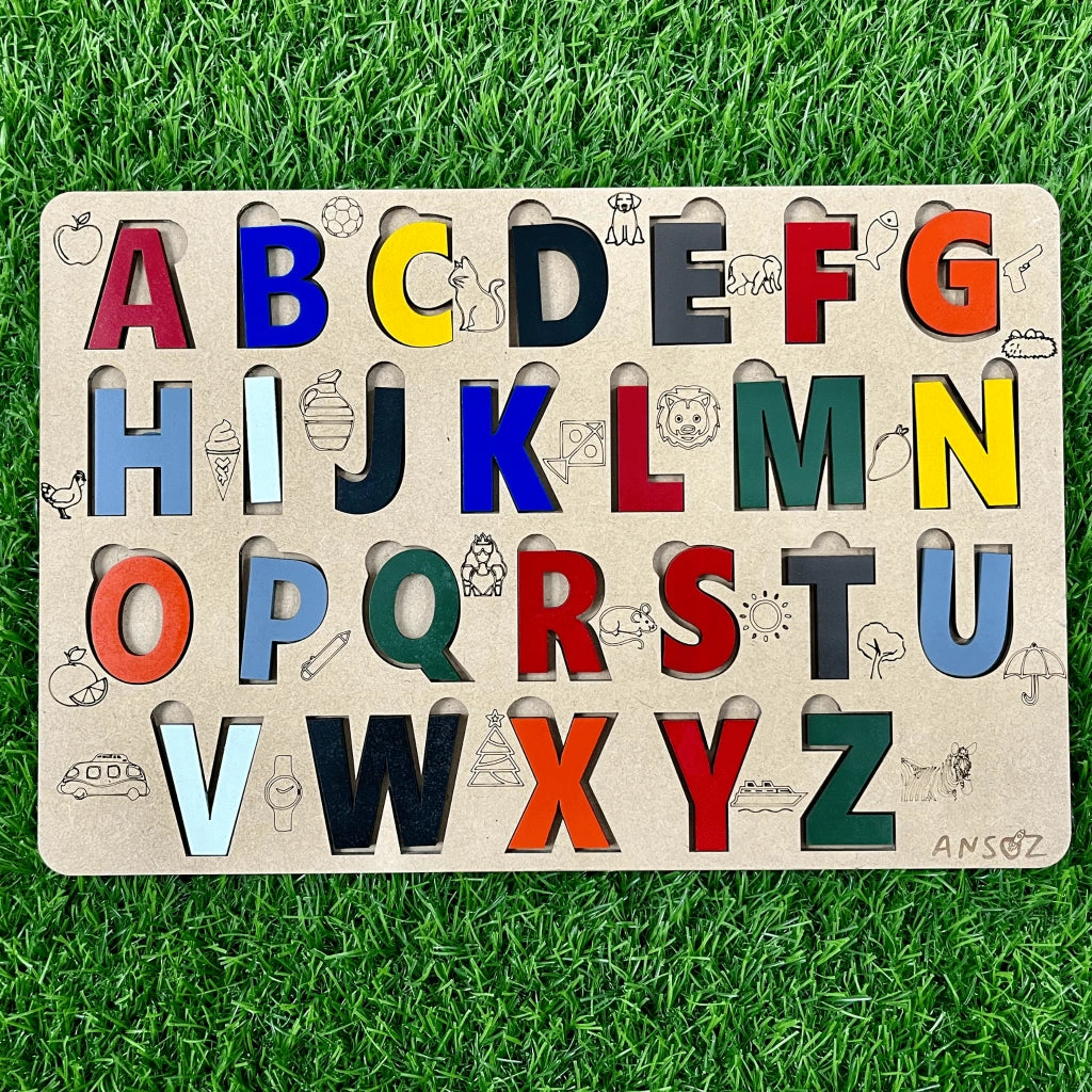 A wooden alphabet puzzle board for children, featuring colorful cutout letters with animal and object illustrations, displayed on a green grass background.