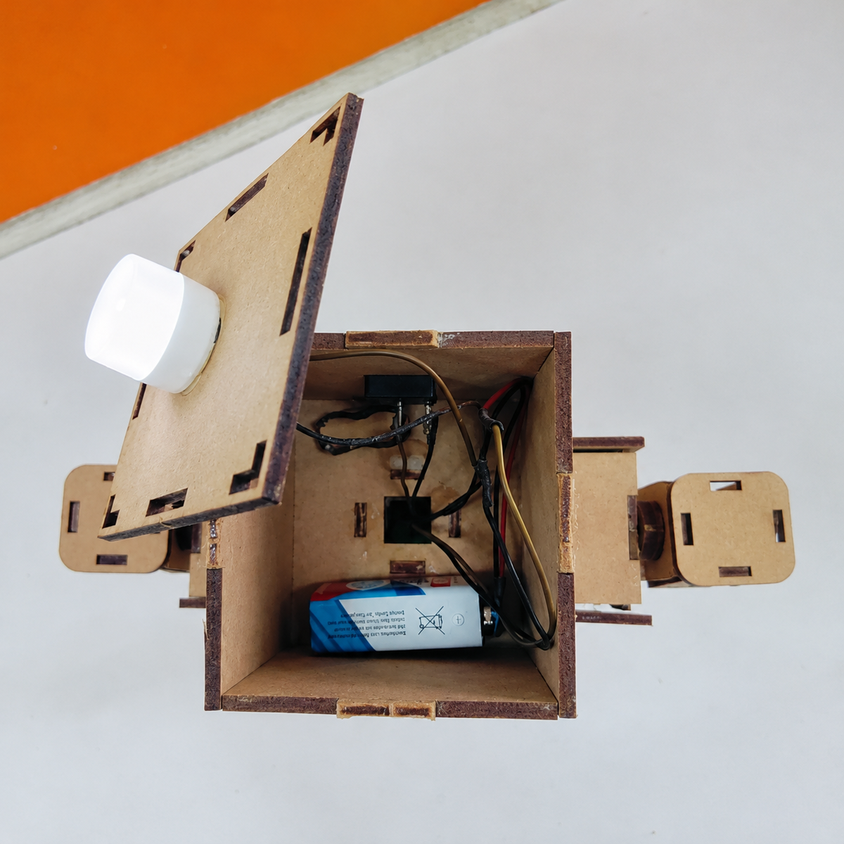 ANSOZ DIY Wooden Light Beam Control Robot Kit showing the internal battery, wiring, and electronic components inside the robot's wooden body for hands-on STEM learning.